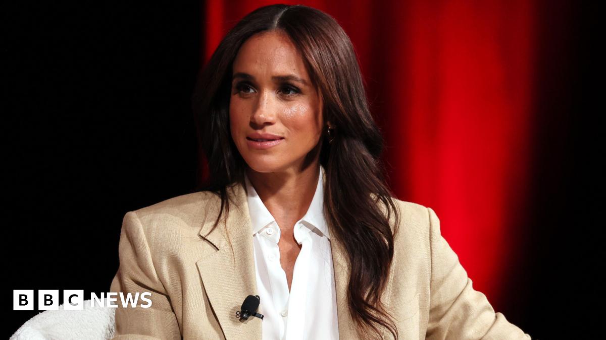 Meghan, the Duchess of Sussex sat down on a white chair wearing a beige suit and white shirt