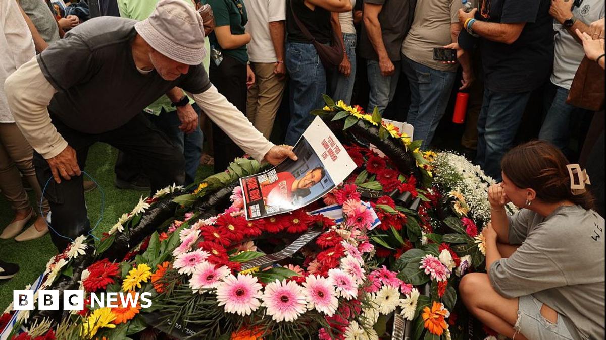 A man holds an image of Tamir Nimrodi, an Israeli soldier who died after being captured on 7 October, above a pile of flowers, surrounded by other mourners