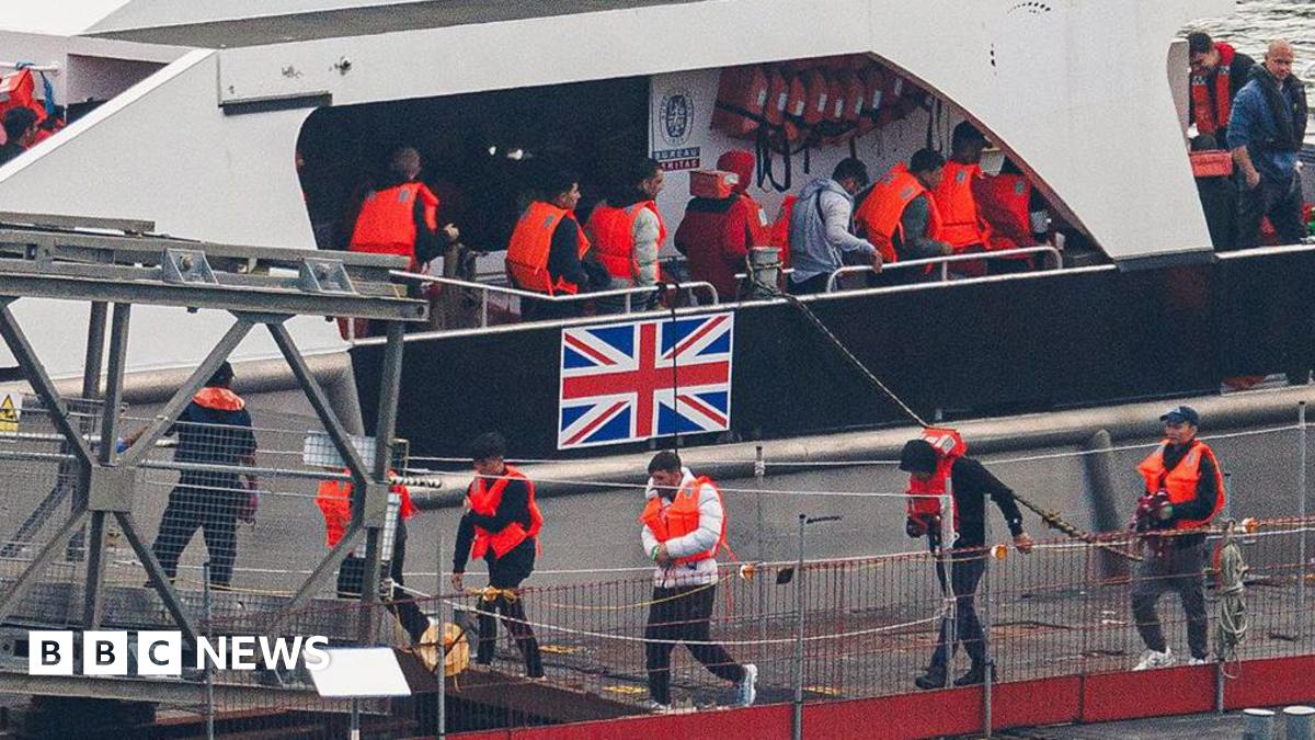 Migrants brought ashore in Dover after attempting to cross the channel. In the background you can see a border force boat with the union flag and migrants being disembarked in Dover at the processing centre known as Jetfoil. 