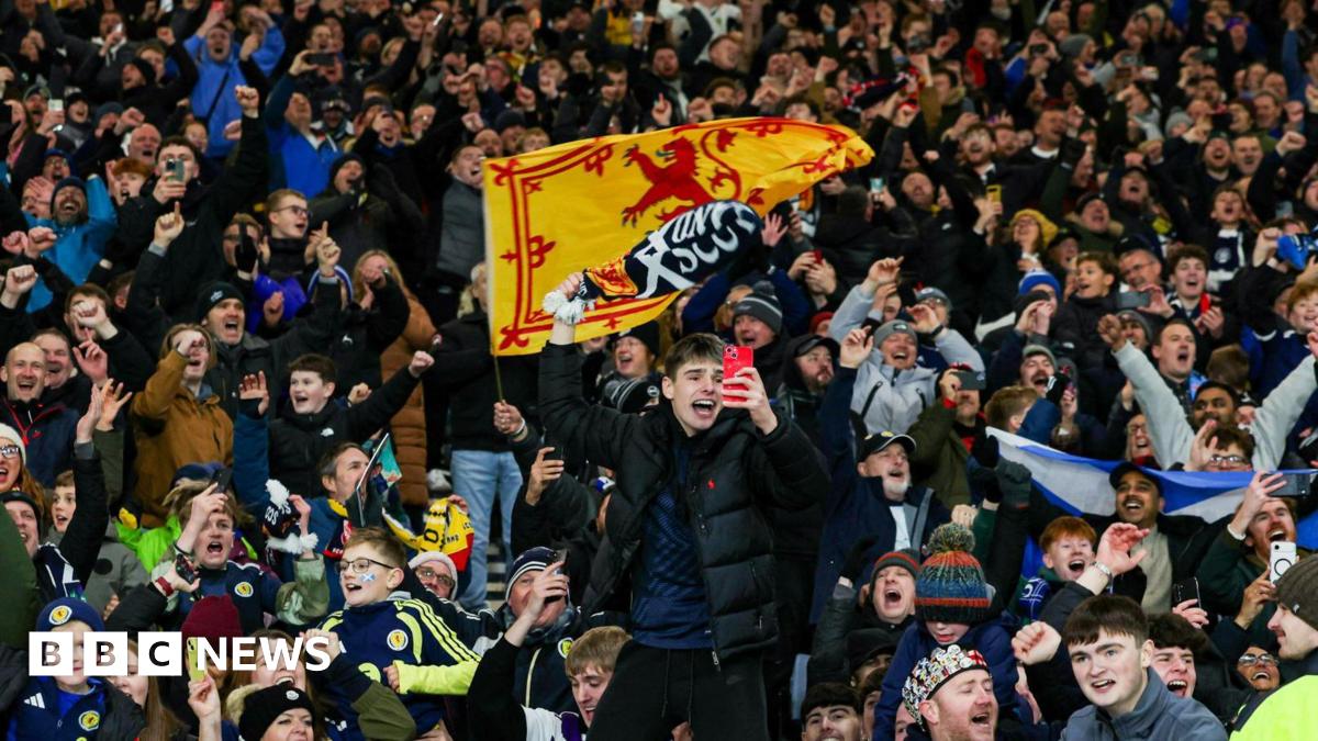 Dozens of Scotland fans celebrating at the final whistle at Hampden. They have scarves and banners.