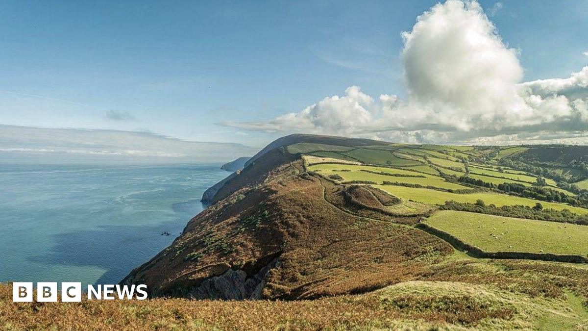 Looking east from Little Hangman to Great Hangman on a fine day, Girt Down, Combe Martin, Exmoor National Park. A sunny day with various vegetation on the coastal section. Blue sea and blue sky with a few white clouds.