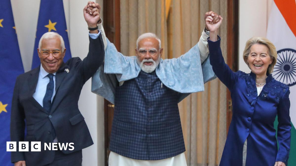 Three leaders hold hands and raise their arms, laughing during a friendly moment. The man in the centre, Indian Prime Minister Narendra Modi, with a white beard and glasses, wears a light shawl over a dark outfit. On either side, European Council Presi...