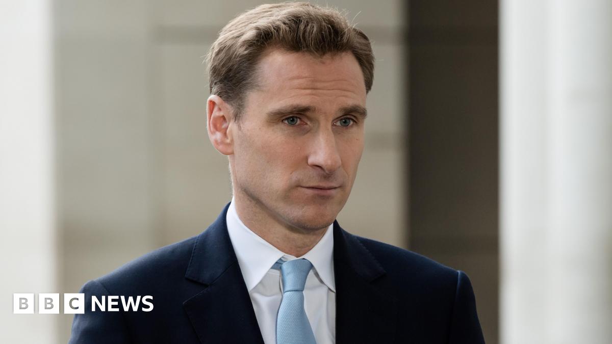 Shadow home secretary Chris Philp, pictured in a dark blue suit and light blue tie. He has a side parting in mousy brown hair and is looking directly forward.