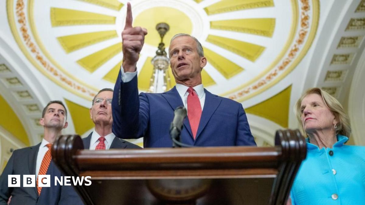 US Senate Majority Leader John Thune stands at a podium in Congress. Three senators stand behind him. 