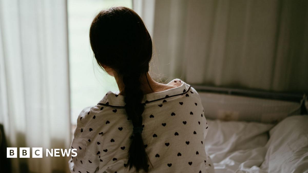 A girl wearing pyjamas sitting on a bed, with her back to the camera