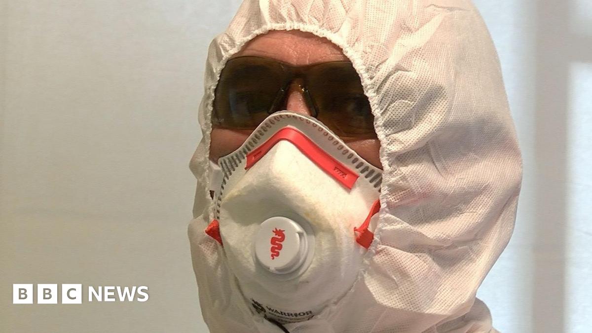 The photo is a close up of trauma cleaner, Jim Gildea's face. There is little skin visible as he's wearing a forensic suit, face mask and protective glasses.