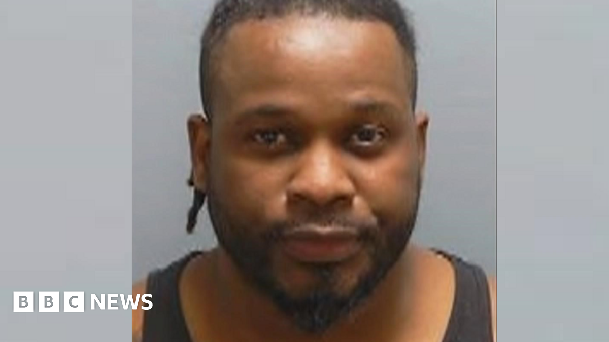 Bruno Sala has a peaked, dark beard and short, dark hair. He wears a black vest in a police custody photo.