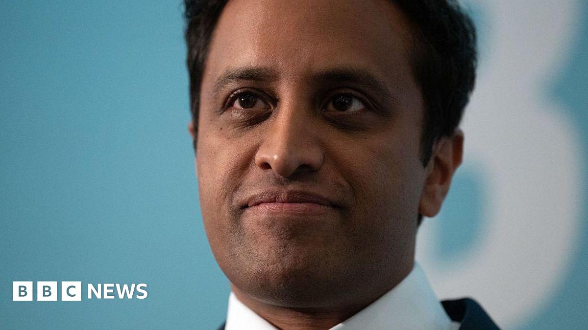 Close shot of former Reform UK chairman Zia Yusuf, wearing a suit, with light blue blurry background