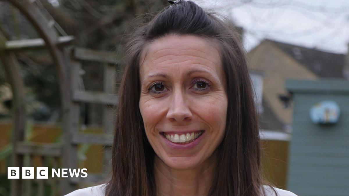 Kristie Higgs smiles at the camera. She has long brown hair down to her shoulders and is wearing a white top