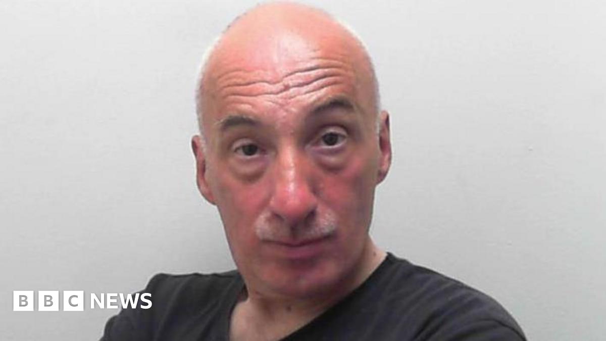 A man with folded arms stares into the camera in a police custody image