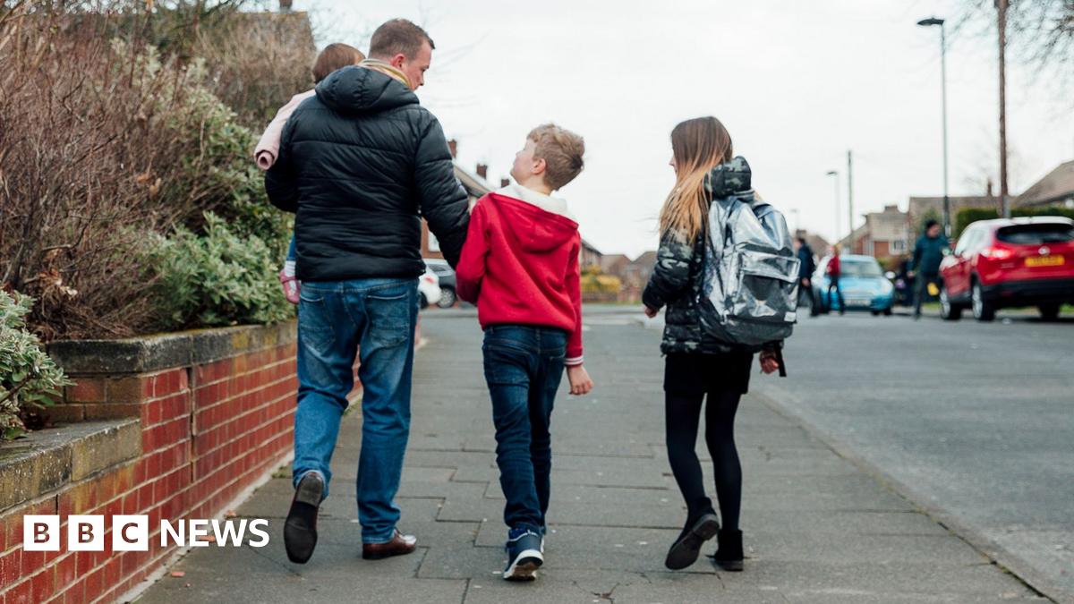 Father with 3 kids walking along the pavement, walking away from the camera. They are on a residential street in the UK 