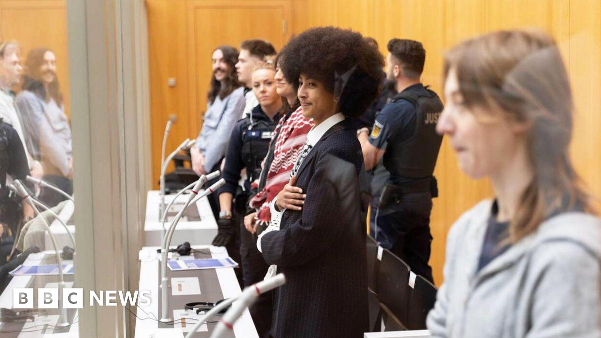 Activists behind glass in the high security prison courtroom. Standing in front of microphones hand cuffed. 