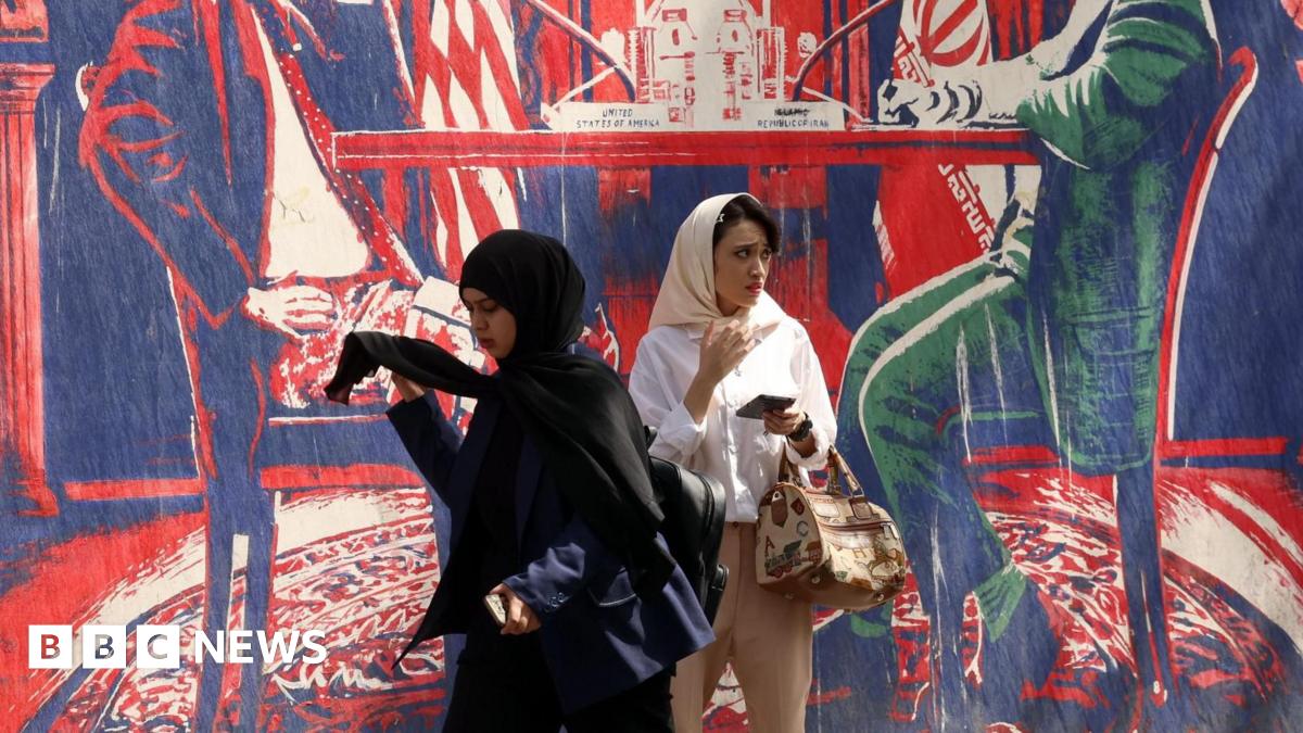 Two women walk next to an anti-US mural near the former US embassy in Tehran