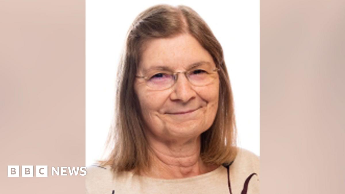 A woman with long light brown hair and wearing glasses looking into the camera. She is wearing a light brown jumper.