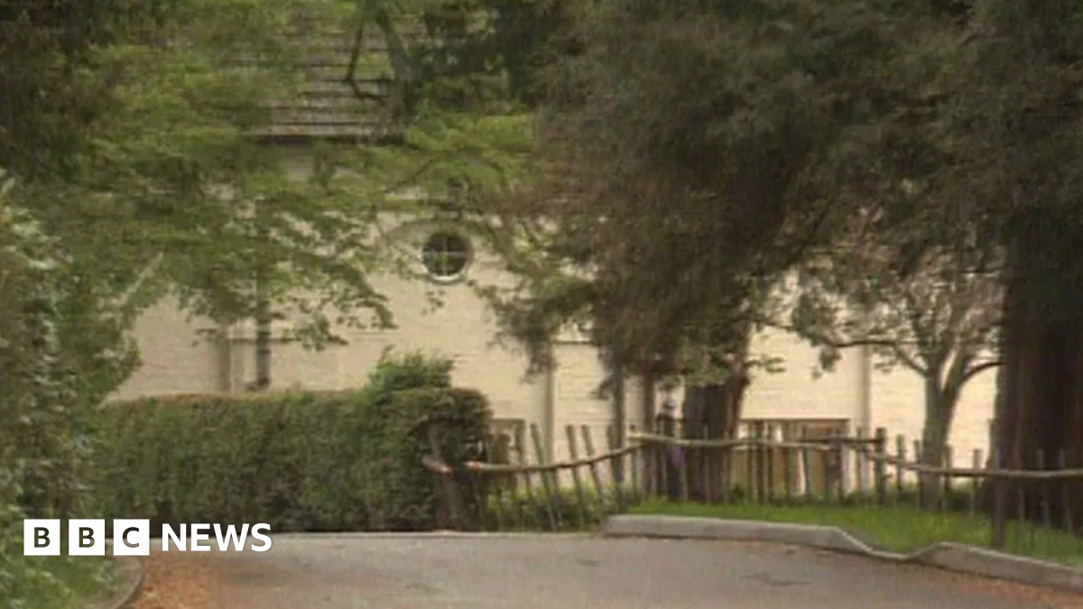 Former Rhydd Court School in Hanley Castle, showing a white building covered by bushes and trees