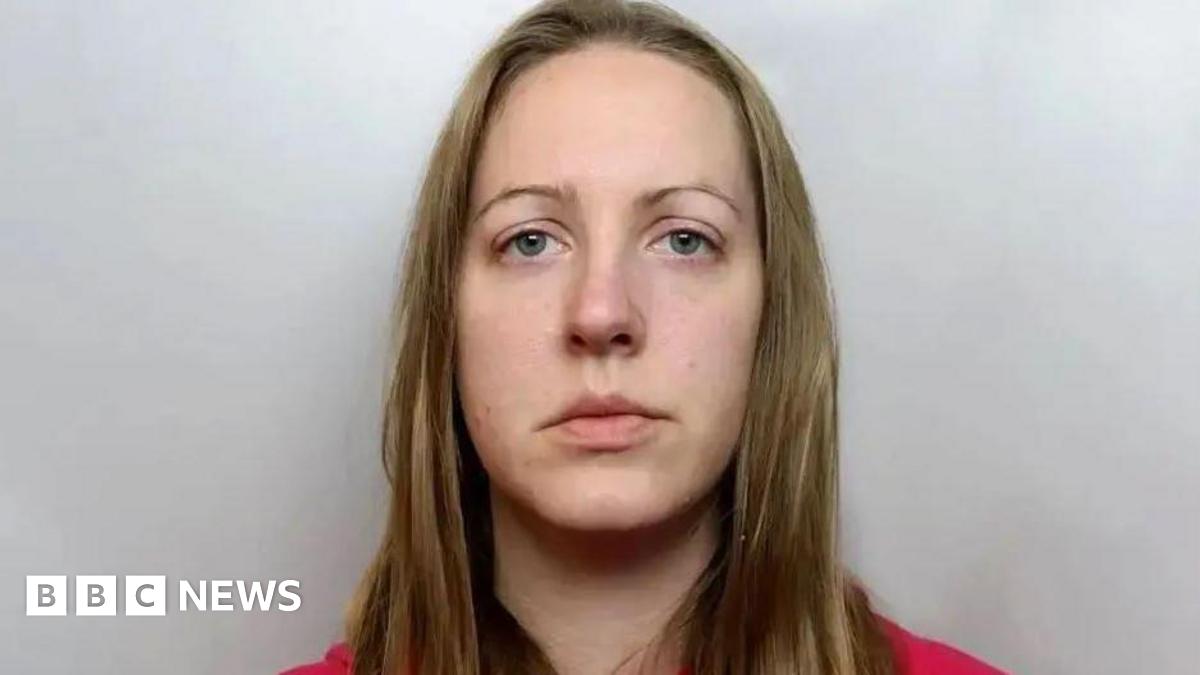 A custody photograph of Lucy Letby, who has long blonde hair and is wearing a red top. She has an impassive facial expression.