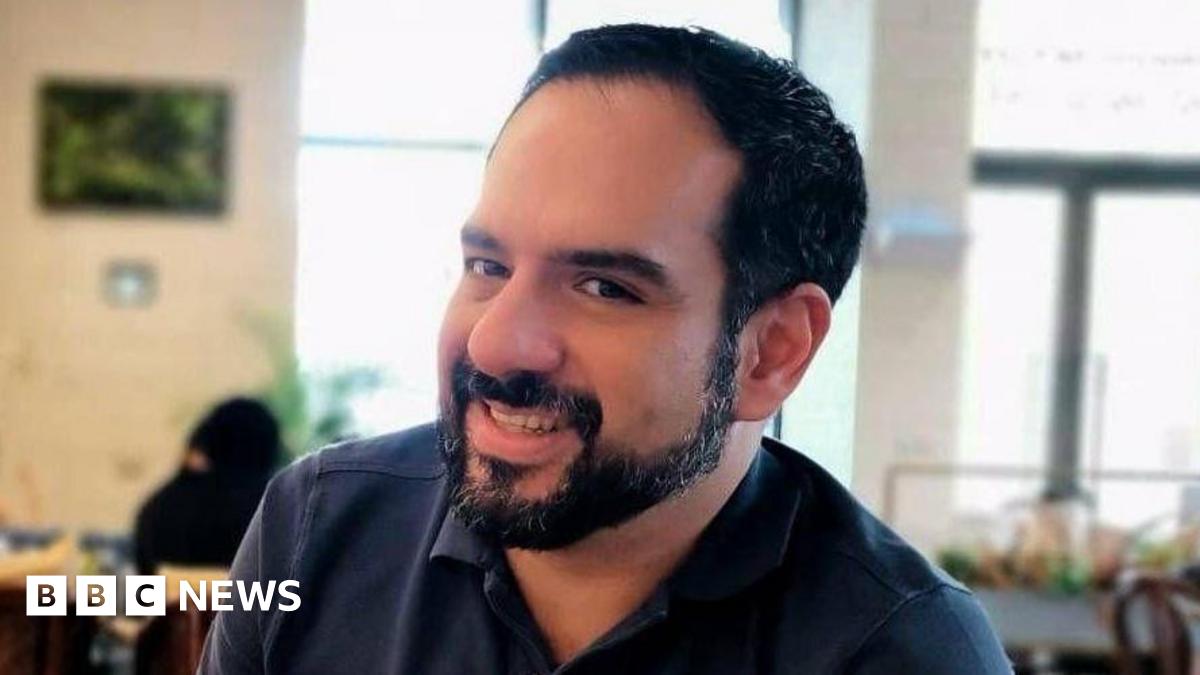 Man with black hair and a beard smiles at camera