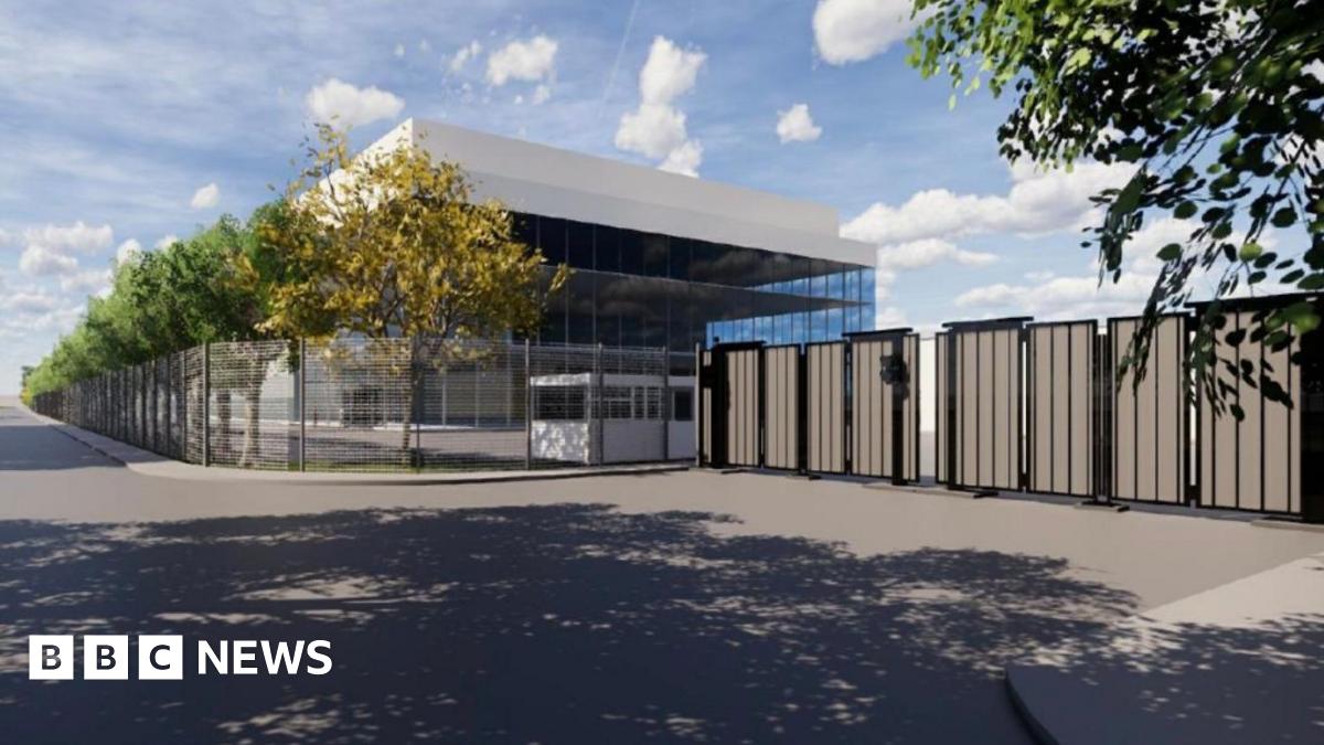 A graphic of what the AI centre will look like. It is a glass building with a white roof. It is surrounded by fencing and trees line its side. There is a road on the other side of the fences.