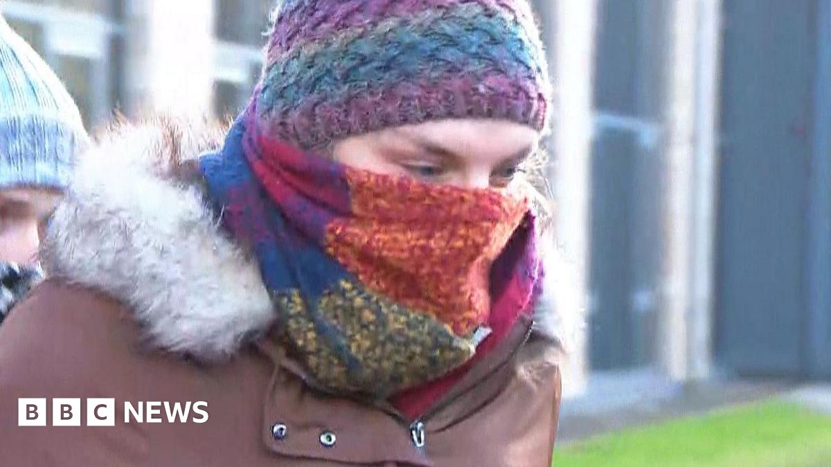 Dr Beth Upton is shown wearing a brown fur-lined jacket while leaving the tribunal office in Dundee. The doctor's face is hidden by a multi-coloured scarf and a purple and blue bobble hat. 