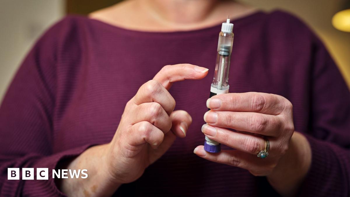 A woman in a burgandy top holds a weight loss injection pen