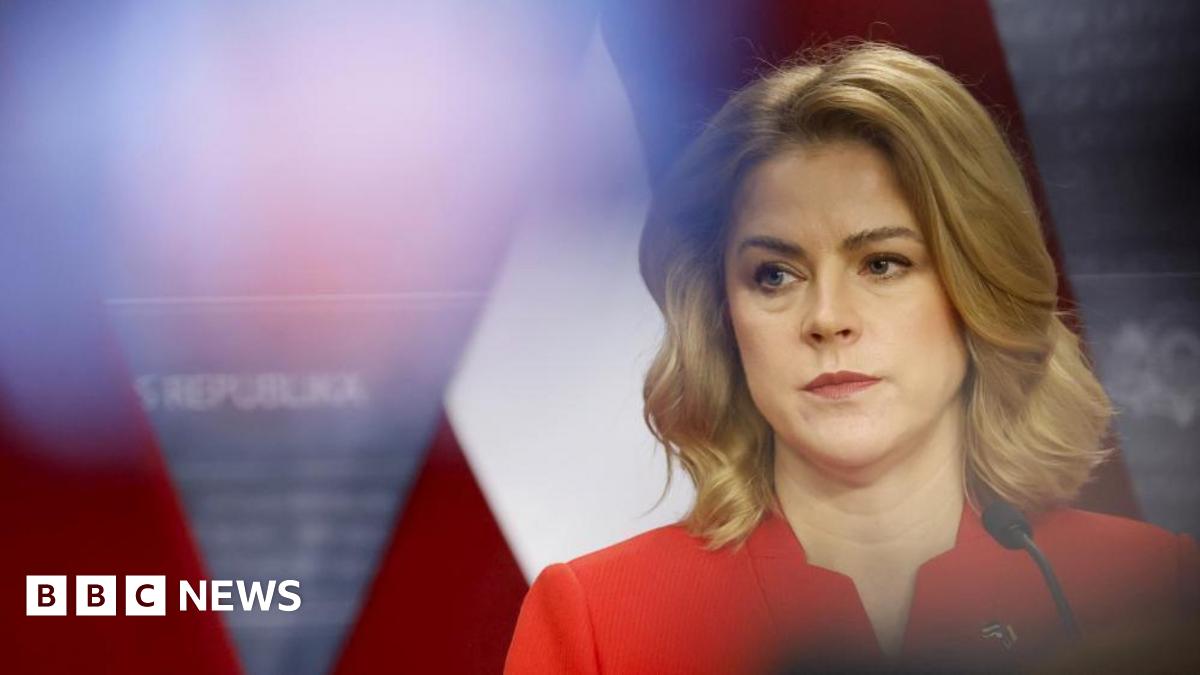 A woman with blonde hair and a red jacket looks ahead with a thoughtful expression