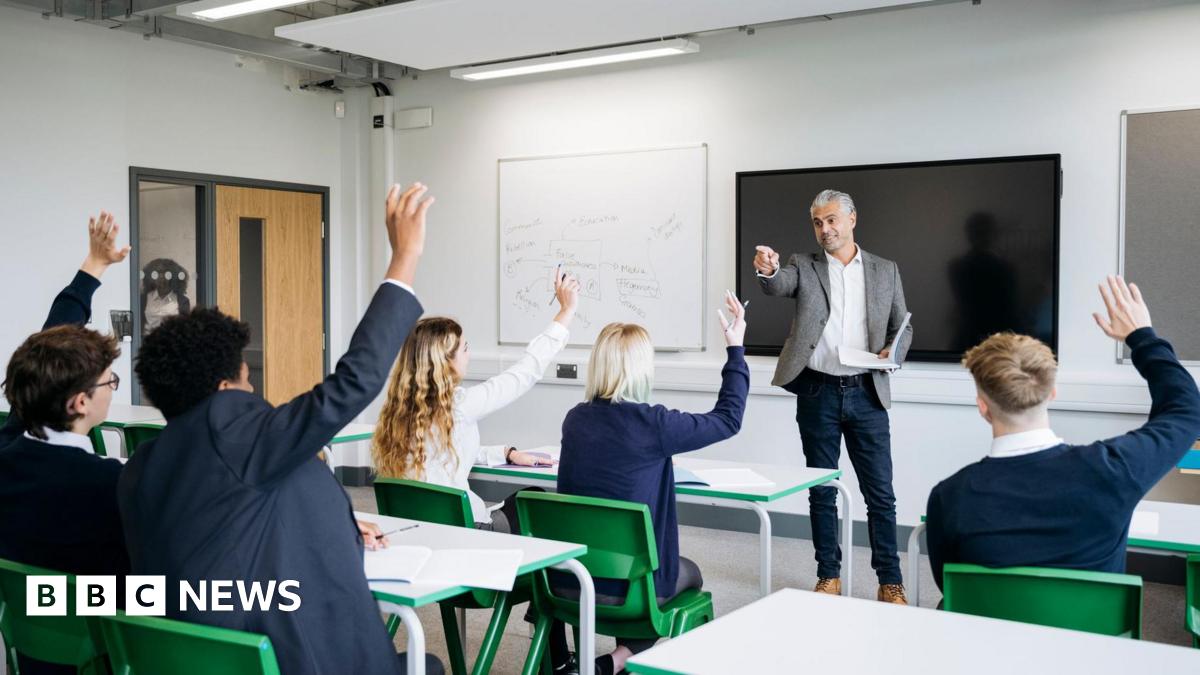 A classroom full of school children in a lesson with a teacher at the front of the class