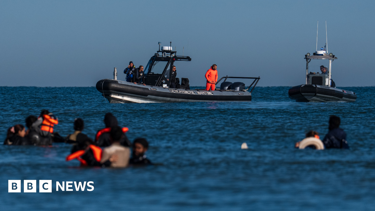 French police vessels look on as migrants wade into the sea to try and board a dinghy to cross the English Channel