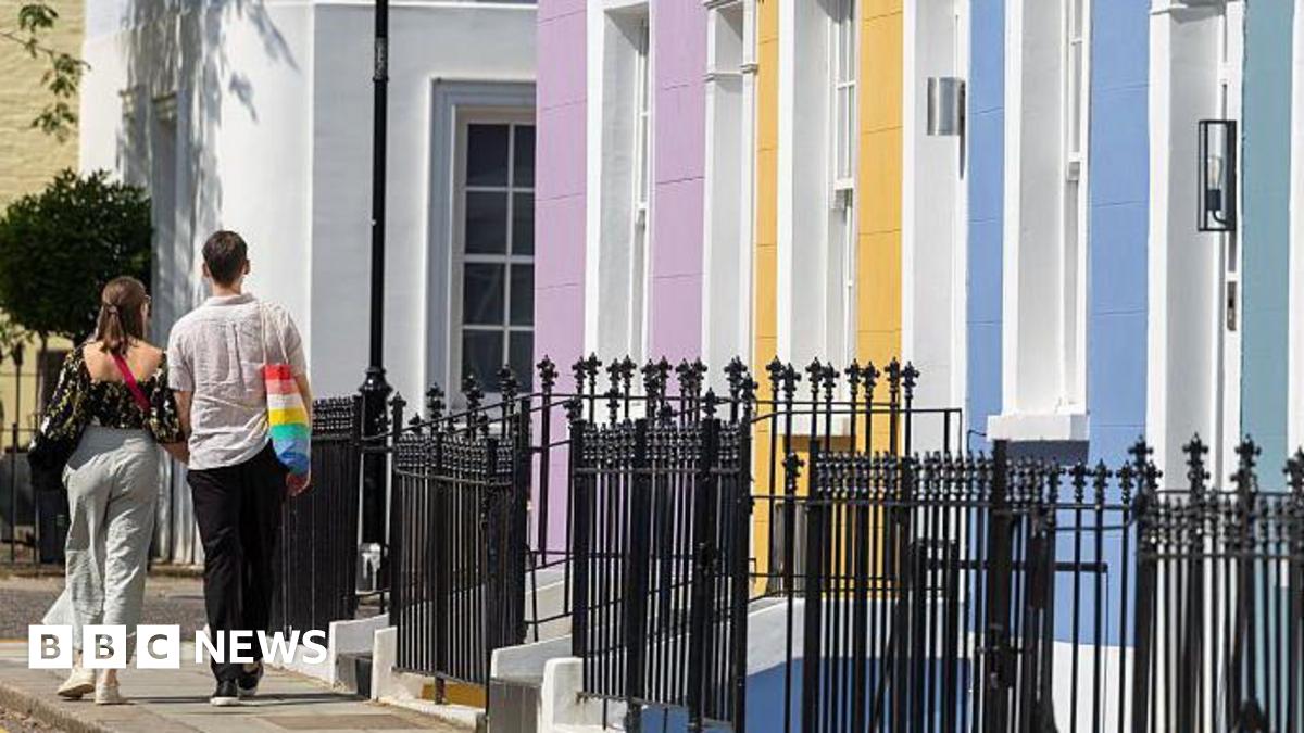 A couple photographed from behind walking down a residential street past houses painted pink, yellow and blue