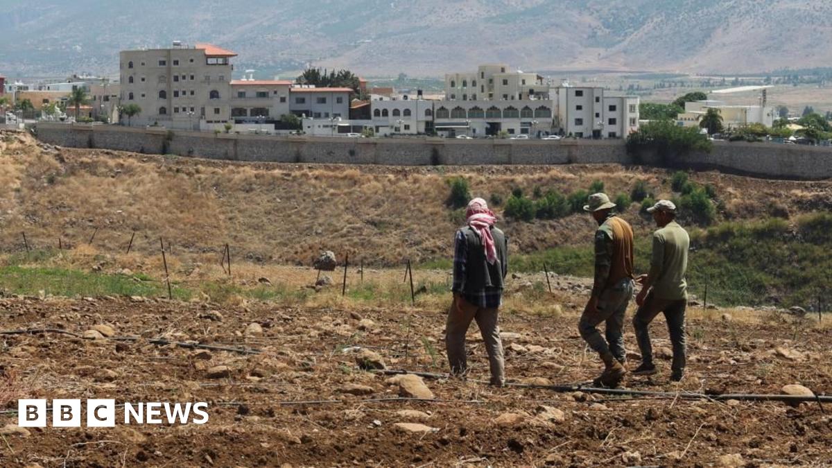 Three farmers walking in soil across a field in southern Lebanon, with a long wall and buildings in the background (file photo)