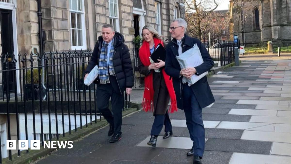 David Toshack on the right of a group of three people wearing a dark suit with a dark jacket.