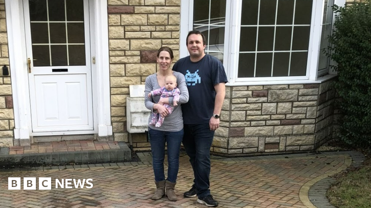 Simon and Louise walker holding their baby in front of their house