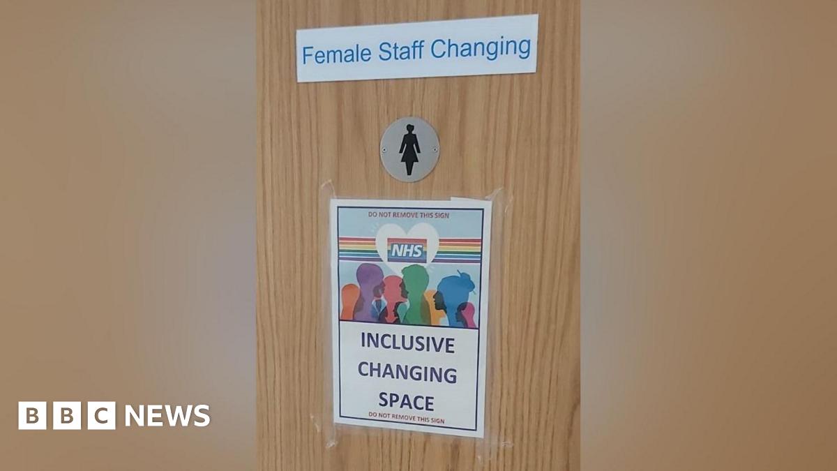 Several signs on a brown wooden door. The top one reads "female staff changing" in blue letters on a white background. beneath is a silver disc with the black shape of a woman. At the bottom is a sheet of A4 with a rainbow NHS logo and the words "inclu...
