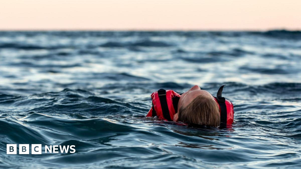 A person lying in open water wearing a red life vest
