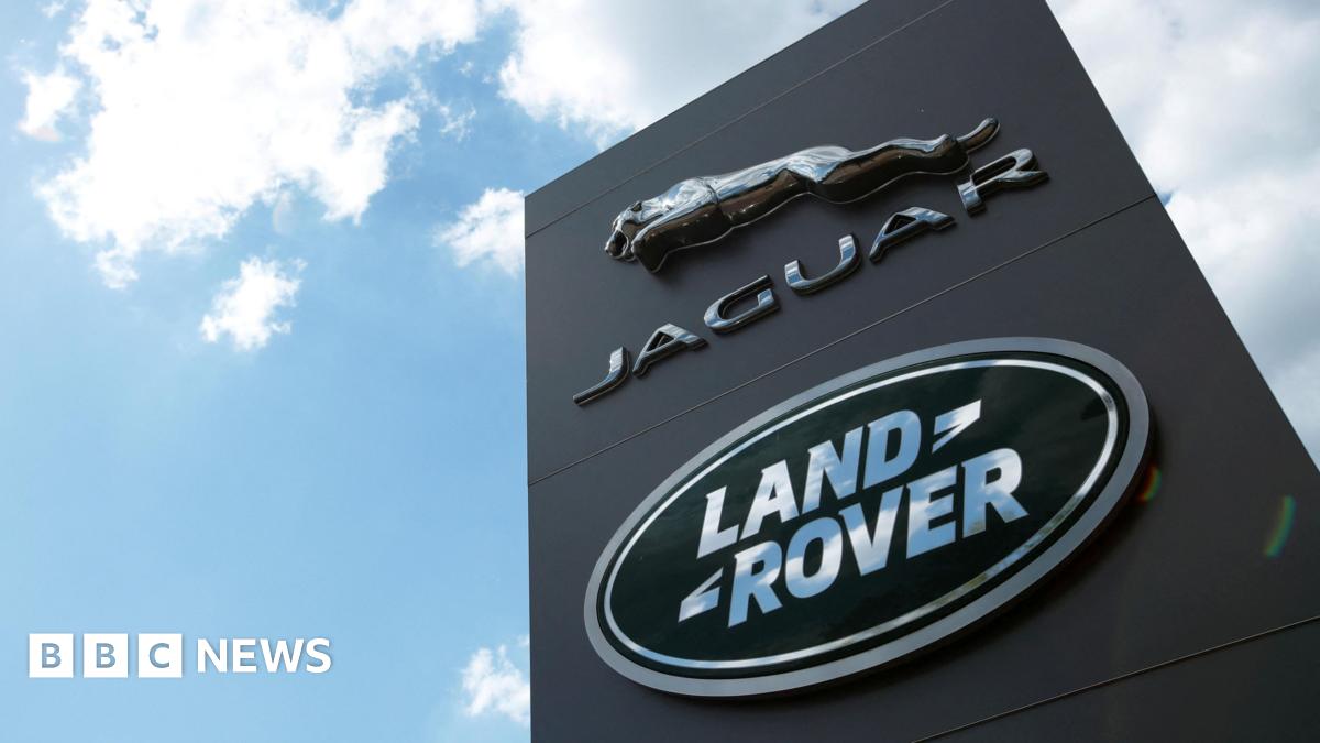A shot looking up at a black sign with the Jaguar and Land Rover logos on, set against a blue sky with clouds.