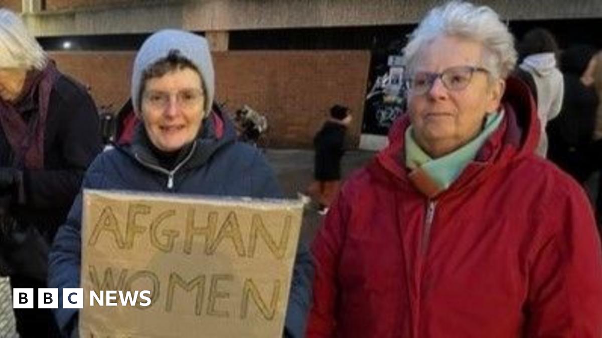 Two women, one in a blue coat and a hat holding a sign that reads 'Afghan women'. The other woman is in a red coat, and she has short white hair