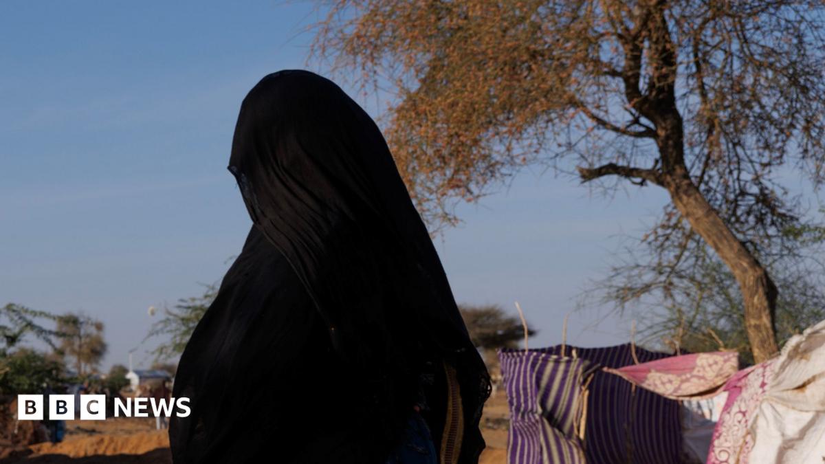 An unidentified woman wearing an abaya and hijab walks through a camp in Chad. Her face is not visible.