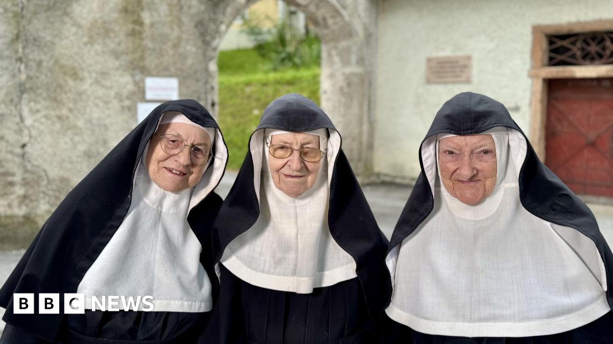 Three nuns stand in front of the monastery in their habits, with Sister Rita on the left and Sister Regina in the centre both wearing glasses