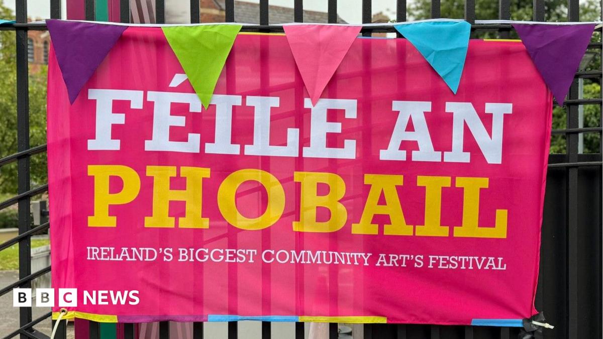 A pink poster with white and yellow writing which says Féile an Phobail on it against black railings 