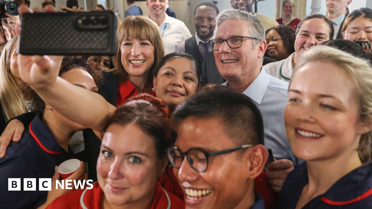 Close up Sir Keir Starmer and Rachel Reeves posing for a selfie taken by an NHS staff member. They are smiling and surrounded by a group of NHS staff all smiling at the camera