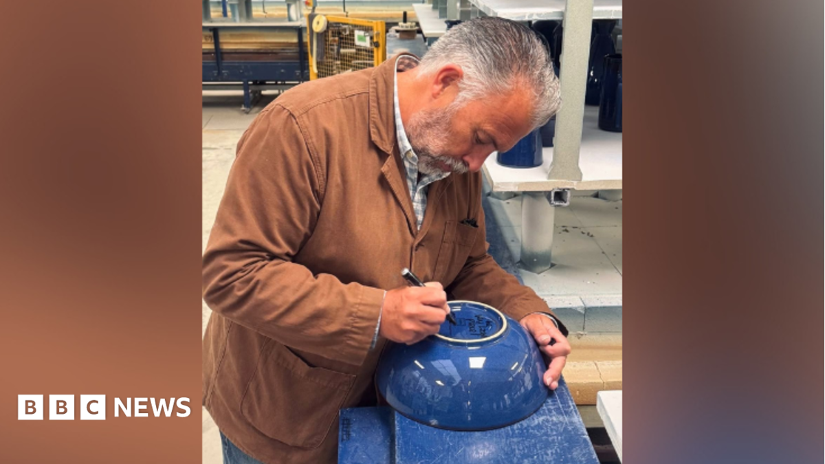 A man in brown jacket signing a blue bowl