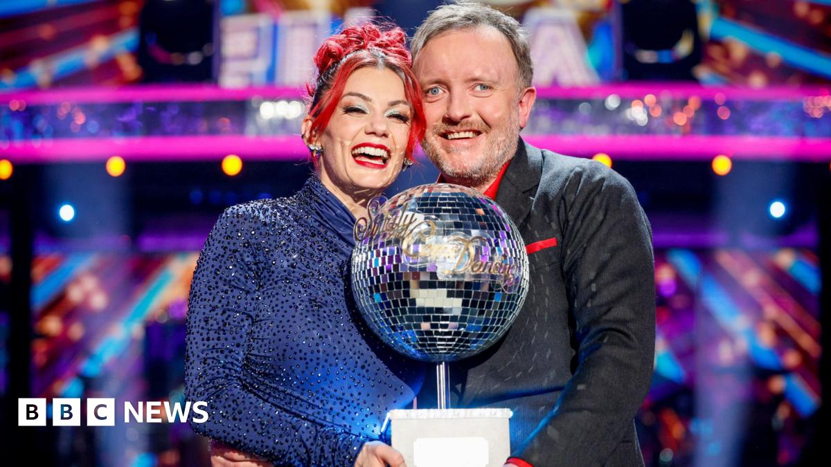 Dianne Buswell and Chris McCausland standing together, smiling and holding the glitterball trophy after winning the Strictly Come Dancing final