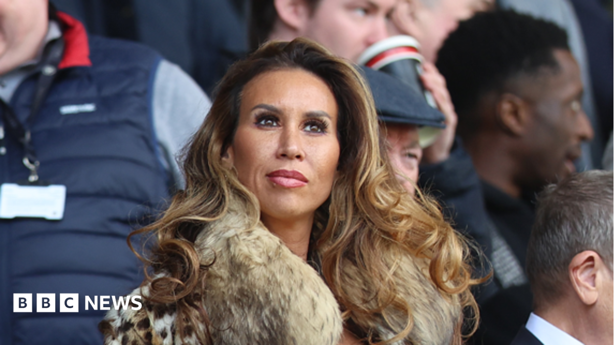 Ampika Pickston has long curled brown hair and is wearing a fur jacket.