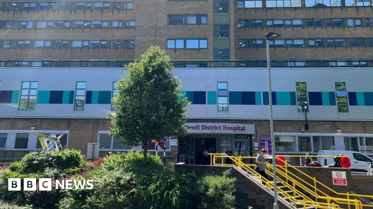 Outside of Yeovil district hospital's main entrance, with yellow steps and green bushes. The building is brown bricks