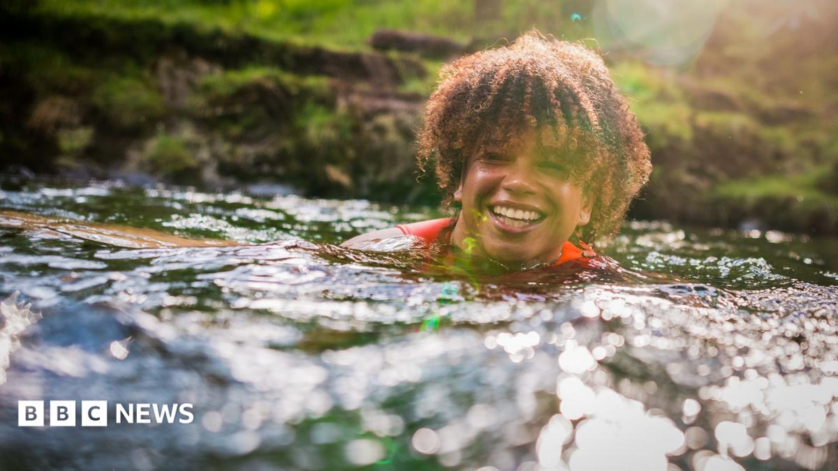Cheerful young woman splashing water while enjoying swim with friends in sea on sunny day