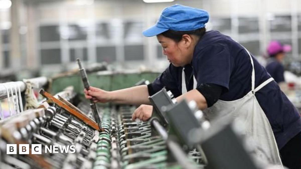 A female worker works on a spun silk production line at a Chinese factory. She is wearing a blue cap and a white apron over her navy blue uniform.