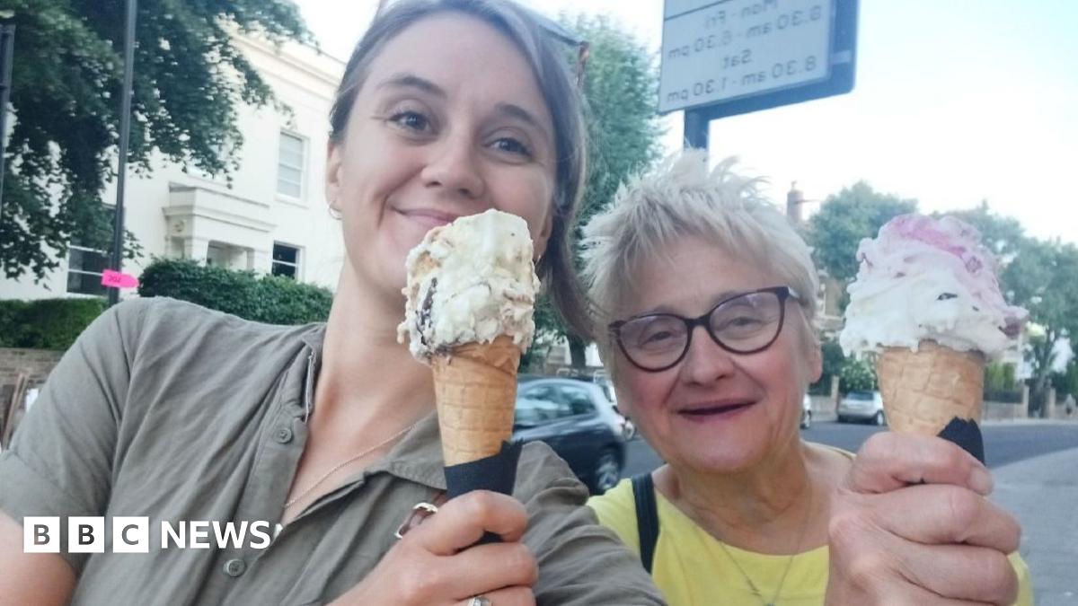 Cat Rubens and Jane Rubens holding ice creams and smiling. Cat is wearing a green button up shirt and sunglasses, while Jane is wearing a bright yellow t-shirt and glasses.