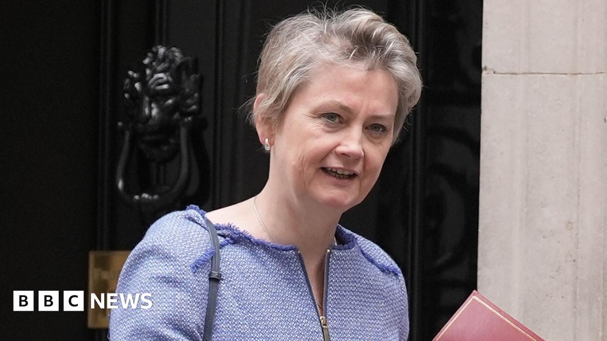 Home Secretary Yvette Cooper looks towards the camera while wearing a blue top with cropped short hair outside Number 10 Downing Street, holding a red file just in view, in London in July.