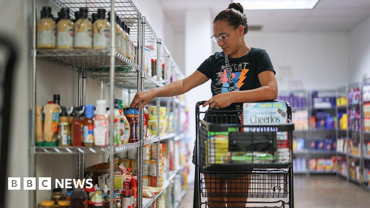 Woman rolls shopping cart down food pantry aisle 