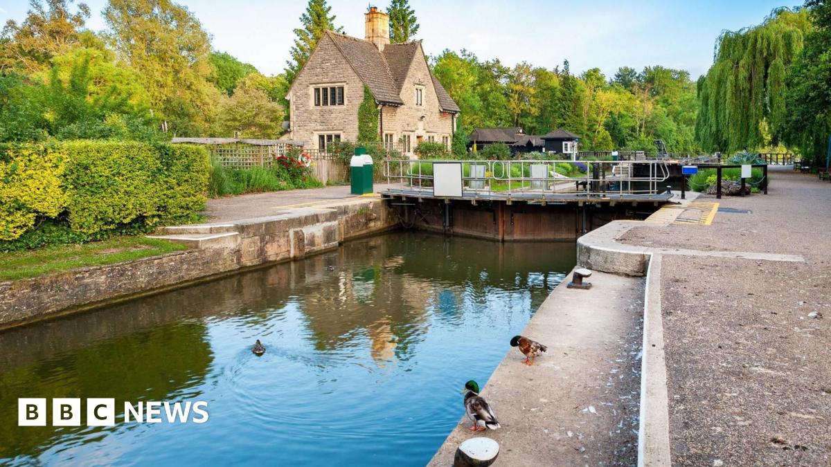 Iffley Lock, with a house in the background and two ducks standing on the side of the lock. Another duck is in the water