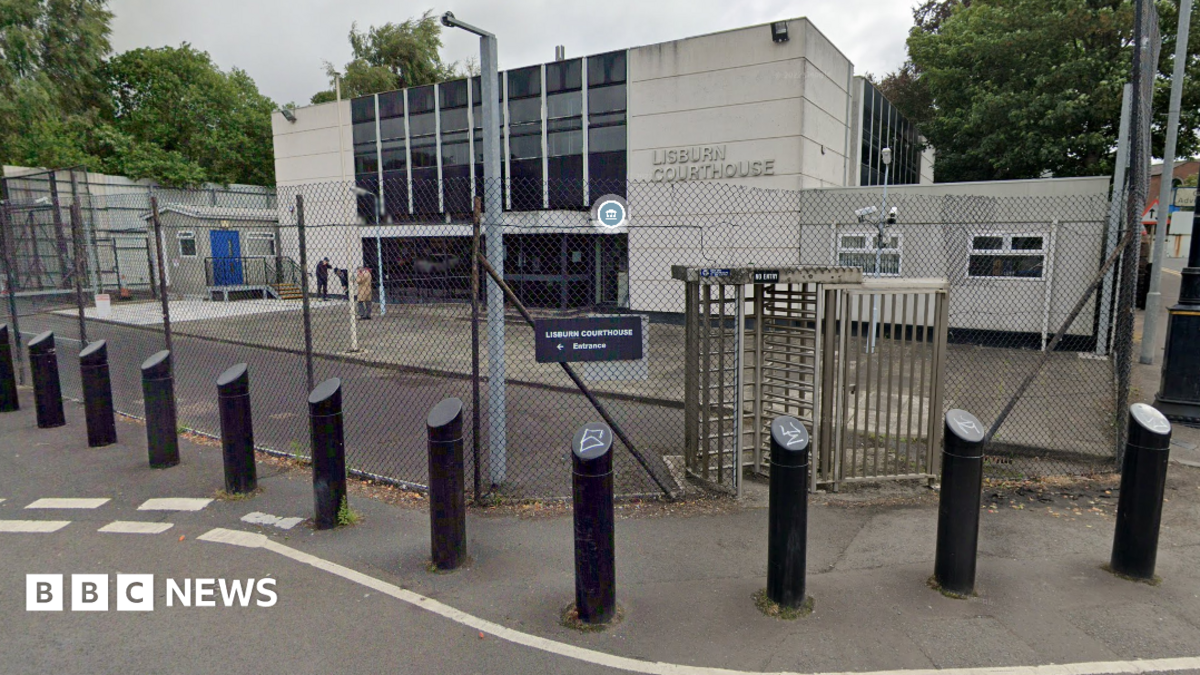 Lisburn Magistrates Court - a white building with doors and windows in the middle. There is a fence, a turnstile and bollards around it. 